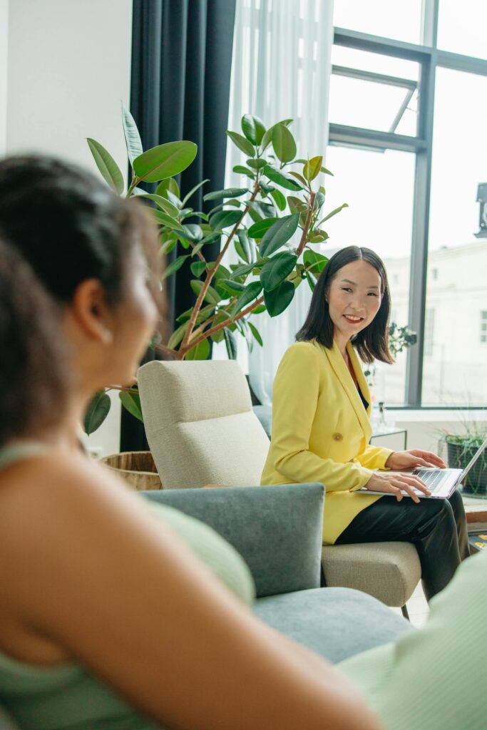 Two women enjoying a casual conversation in a bright, plant-filled modern office.